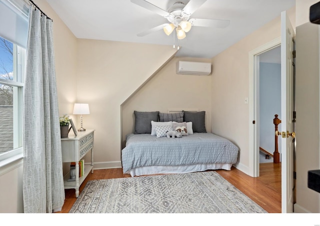 bedroom with a ceiling fan, a wall mounted air conditioner, baseboards, and wood finished floors