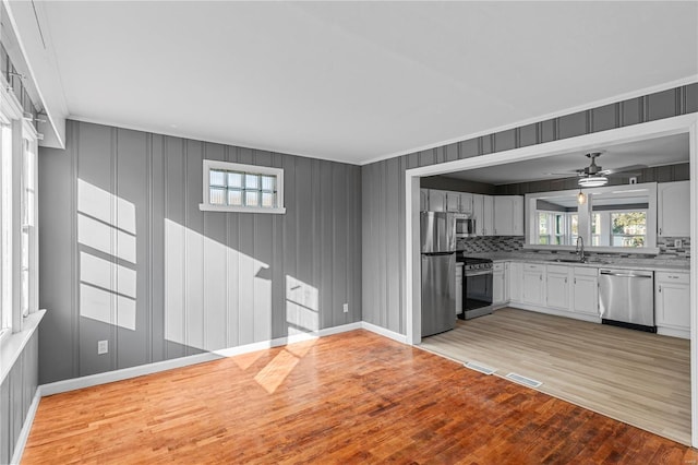 kitchen with sink, decorative backsplash, light wood-type flooring, white cabinetry, and stainless steel appliances