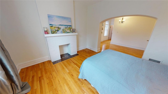 bedroom featuring wood-type flooring, an inviting chandelier, and a brick fireplace