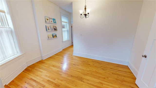 empty room featuring a chandelier, light hardwood / wood-style floors, and a healthy amount of sunlight