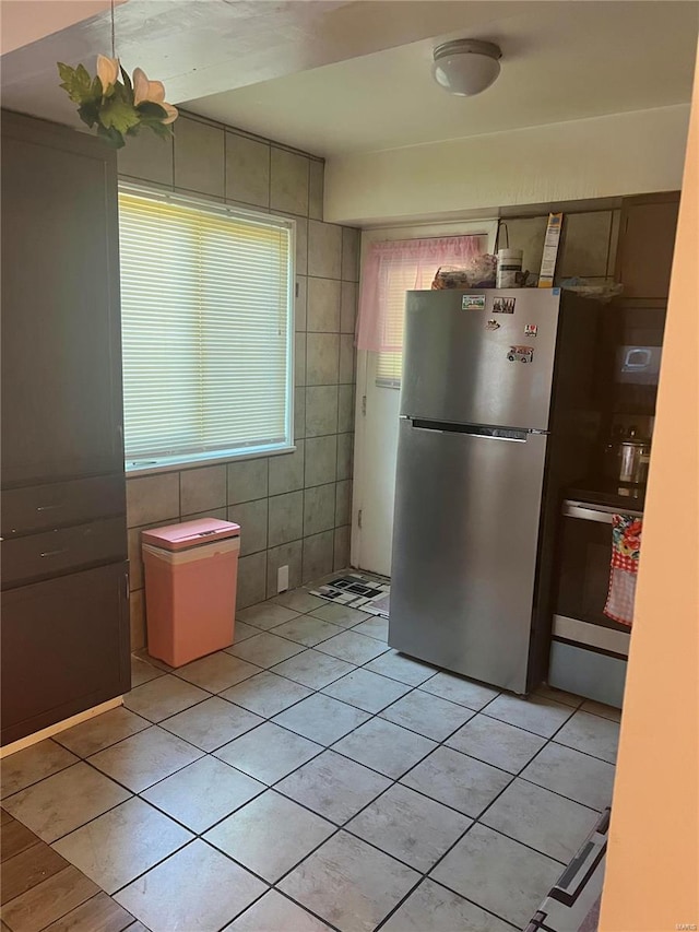 kitchen with light tile patterned floors, tile walls, appliances with stainless steel finishes, and an inviting chandelier