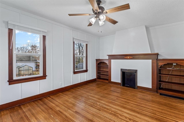 unfurnished living room featuring hardwood / wood-style floors, a textured ceiling, a large fireplace, and ceiling fan