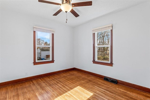 empty room featuring a wealth of natural light, ceiling fan, and hardwood / wood-style flooring