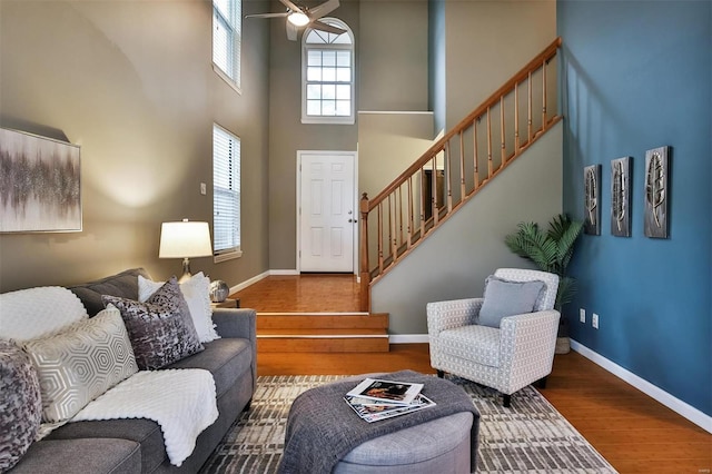 living room featuring wood-type flooring, ceiling fan, and a high ceiling