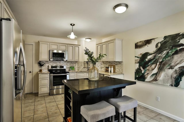 kitchen with backsplash, hanging light fixtures, appliances with stainless steel finishes, cream cabinetry, and a kitchen bar