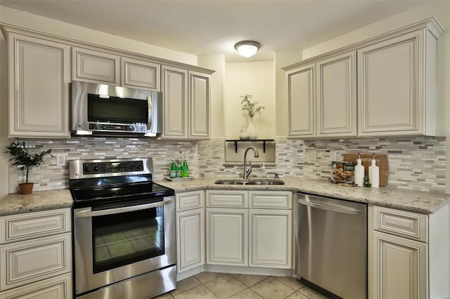 kitchen with decorative backsplash, stainless steel appliances, sink, light tile patterned floors, and cream cabinetry