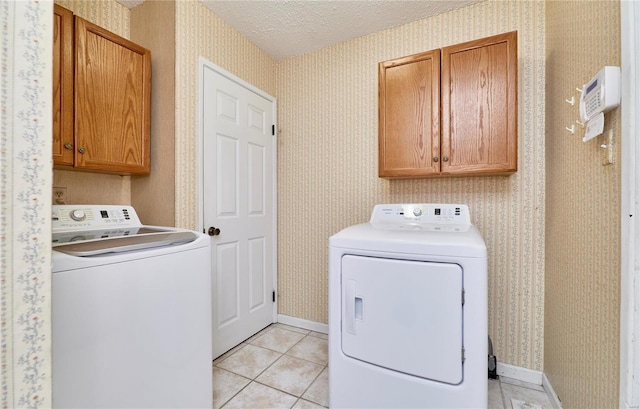 laundry room featuring light tile patterned floors, washer and dryer, a textured ceiling, and cabinets