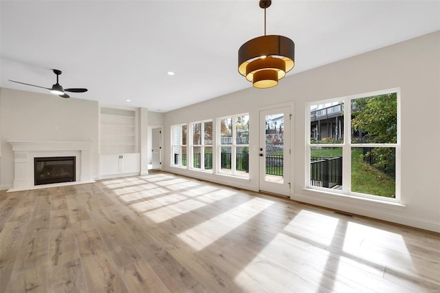 unfurnished living room with ceiling fan, built in features, a wealth of natural light, and light hardwood / wood-style flooring