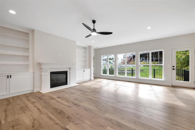 unfurnished living room featuring built in shelves, light hardwood / wood-style floors, and ceiling fan