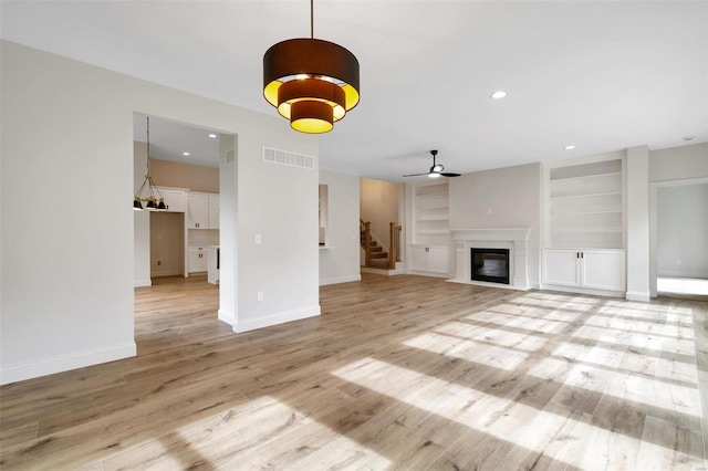 unfurnished living room with ceiling fan, light hardwood / wood-style floors, and built in features