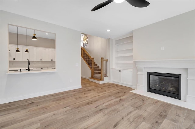 unfurnished living room with light wood-type flooring, built in features, ceiling fan, and sink