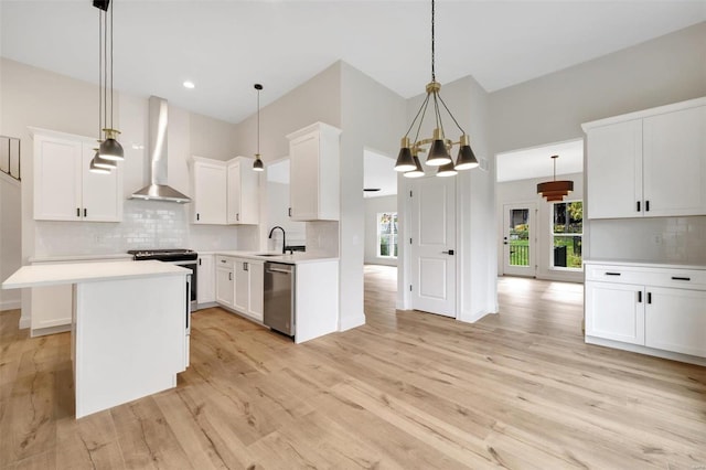 kitchen with pendant lighting, stainless steel appliances, wall chimney exhaust hood, and light hardwood / wood-style floors