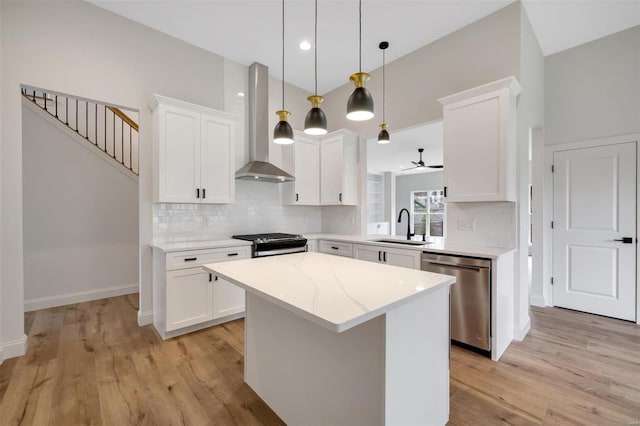 kitchen featuring wall chimney exhaust hood, stainless steel appliances, pendant lighting, white cabinets, and a kitchen island