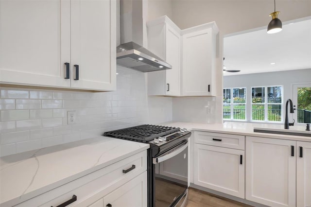 kitchen featuring stainless steel gas range oven, sink, wall chimney range hood, pendant lighting, and white cabinets