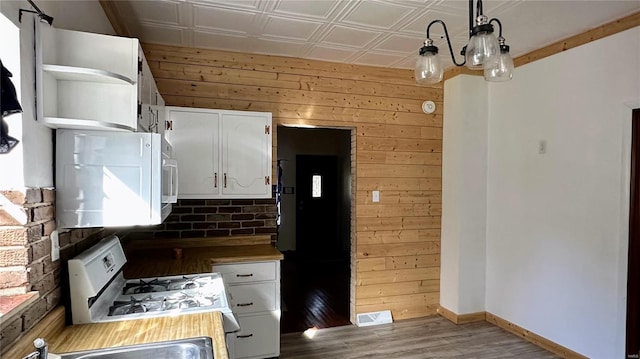 kitchen featuring white cabinets, wood walls, and hanging light fixtures