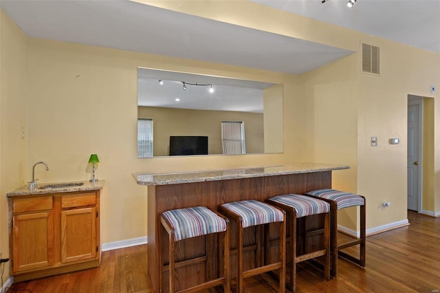 bar with rail lighting, light stone counters, dark wood-type flooring, and sink