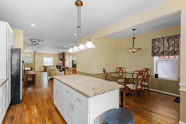 kitchen with white cabinets, a center island, stainless steel refrigerator, and hanging light fixtures