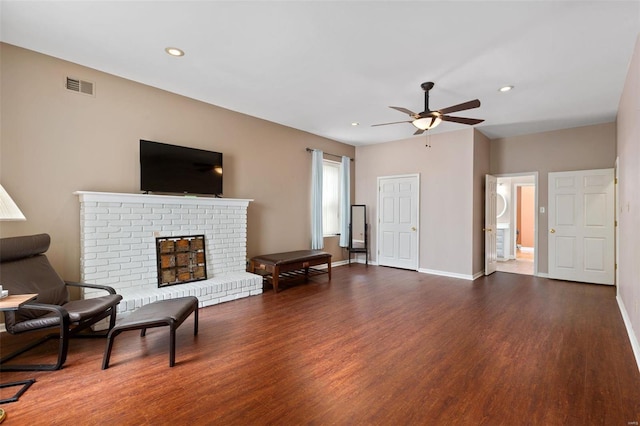 living room featuring ceiling fan, a fireplace, and dark wood-type flooring