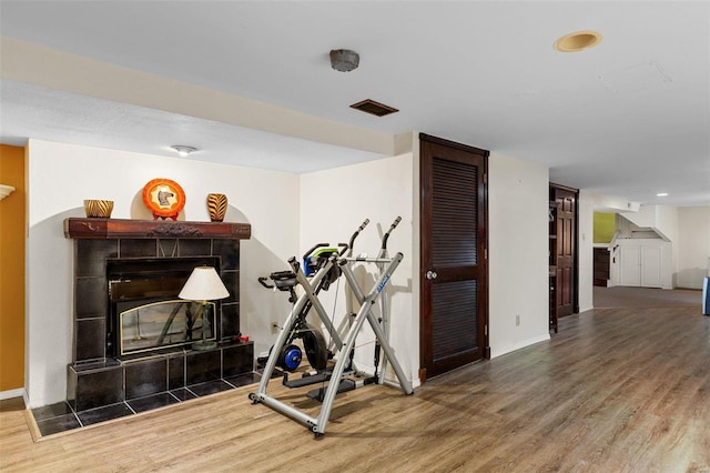 workout room featuring a tile fireplace and hardwood / wood-style floors