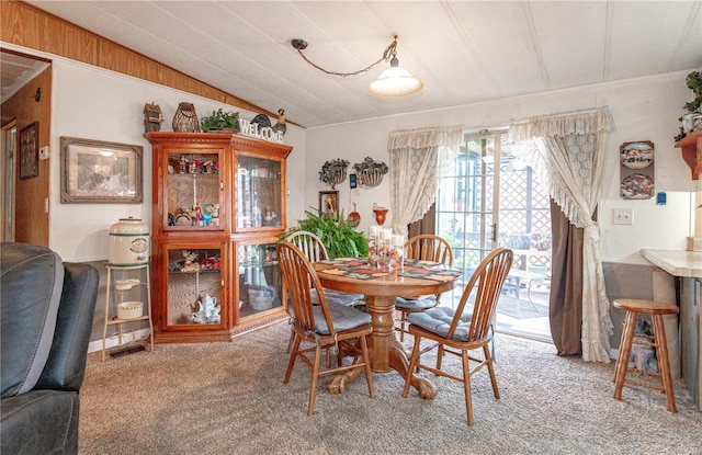 carpeted dining space with vaulted ceiling and wooden walls