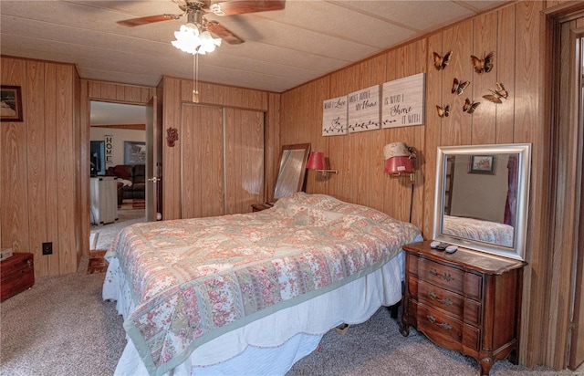 carpeted bedroom with a closet, ceiling fan, and wooden walls