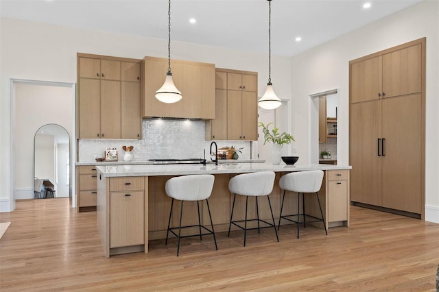 kitchen featuring a kitchen island with sink, hanging light fixtures, light hardwood / wood-style floors, light brown cabinetry, and decorative backsplash