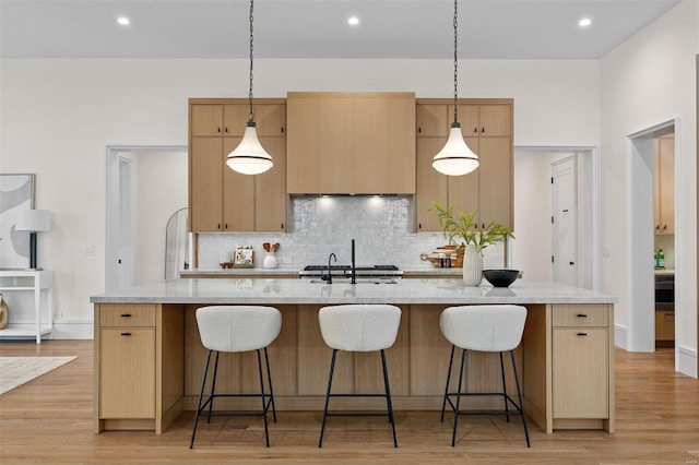 kitchen with decorative light fixtures, light stone countertops, a kitchen island with sink, and decorative backsplash