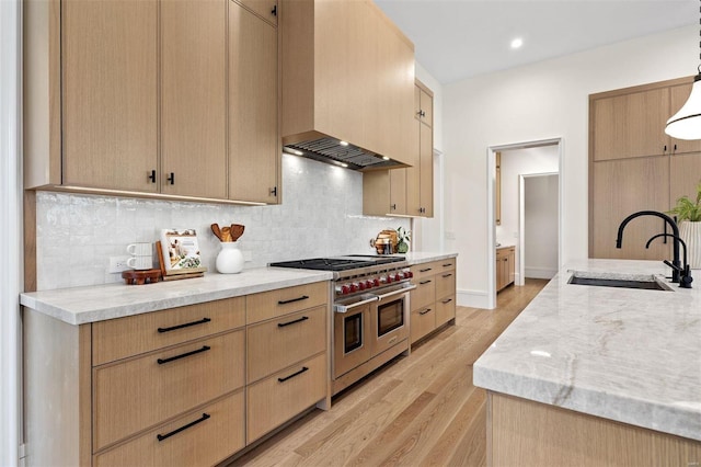 kitchen featuring sink, double oven range, light brown cabinetry, decorative light fixtures, and light wood-type flooring