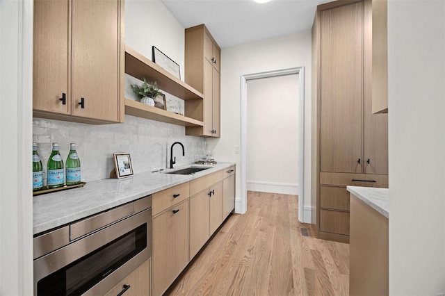 kitchen featuring sink, stainless steel microwave, light brown cabinets, and light wood-type flooring