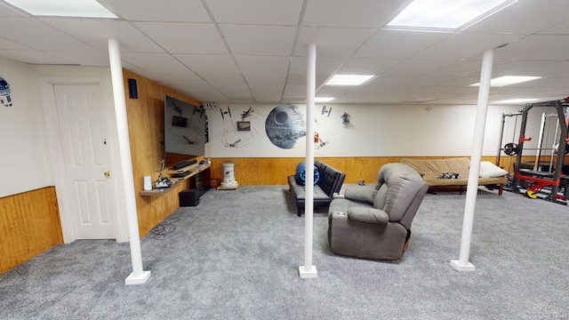 interior space with carpet flooring, a drop ceiling, and wood walls