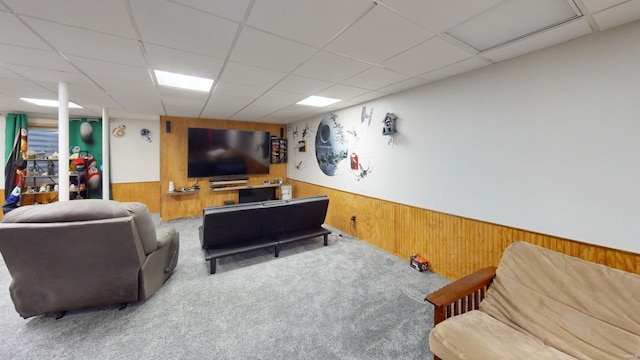 carpeted living room with a drop ceiling and wooden walls