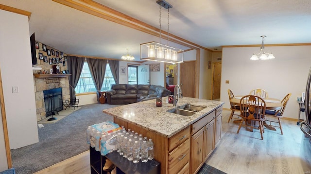 kitchen featuring sink, hanging light fixtures, a stone fireplace, a center island with sink, and ornamental molding