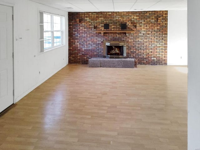 unfurnished living room with a paneled ceiling, light hardwood / wood-style flooring, and brick wall