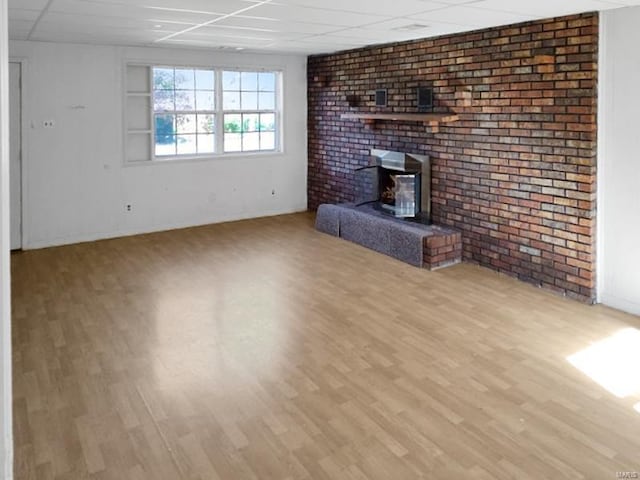 unfurnished living room with light hardwood / wood-style flooring, a wood stove, and brick wall