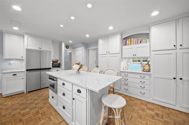 kitchen featuring a breakfast bar, dark parquet floors, stainless steel appliances, white cabinets, and a kitchen island