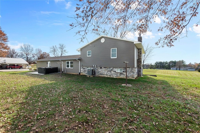 rear view of property featuring a yard, cooling unit, and a hot tub