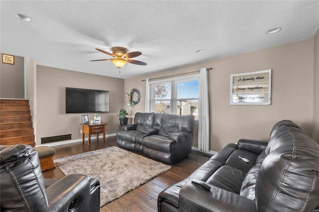 living room with a textured ceiling, ceiling fan, and dark wood-type flooring