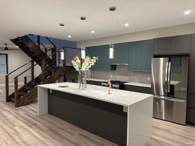 kitchen featuring tasteful backsplash, stainless steel appliances, a kitchen island with sink, decorative light fixtures, and light hardwood / wood-style floors