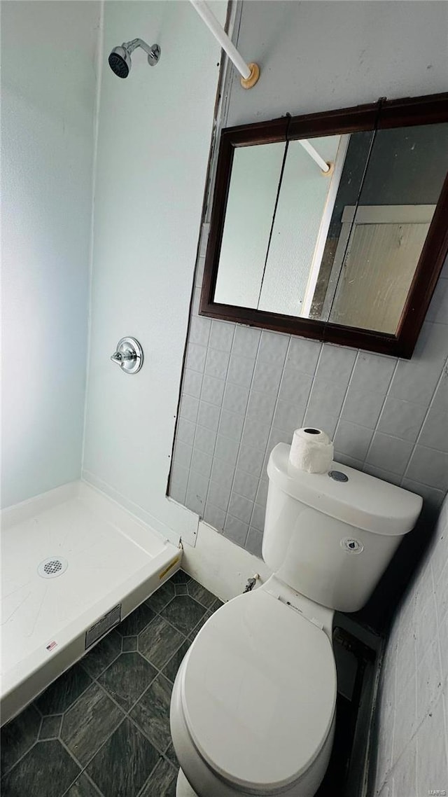 bathroom with tile patterned flooring, toilet, a shower, and tile walls