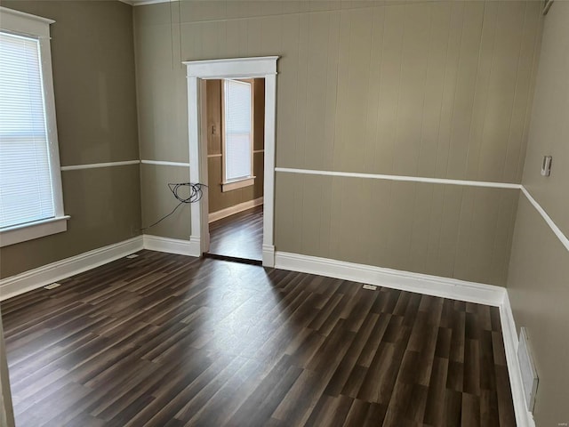 spare room featuring dark hardwood / wood-style flooring, wooden walls, and a healthy amount of sunlight