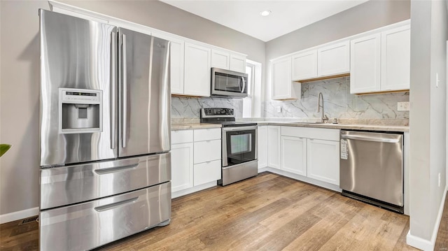 kitchen with a sink, white cabinetry, light countertops, appliances with stainless steel finishes, and backsplash