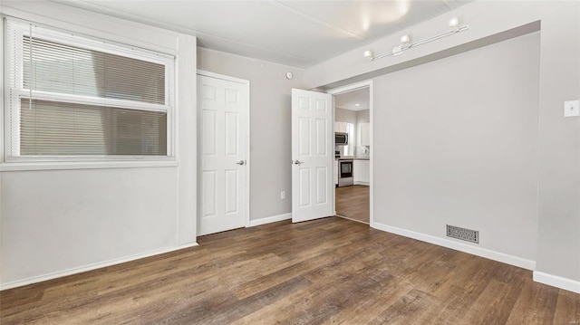 spare room with dark wood-style floors, visible vents, and baseboards