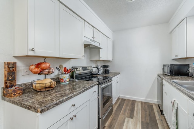 kitchen with appliances with stainless steel finishes, dark stone counters, a textured ceiling, dark wood-type flooring, and white cabinets