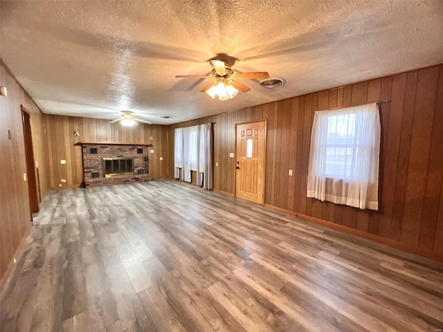 unfurnished living room featuring hardwood / wood-style flooring, wooden walls, and a brick fireplace