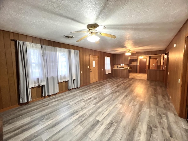 unfurnished living room featuring light hardwood / wood-style floors, ceiling fan, and wood walls