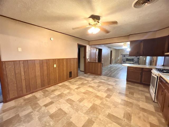 kitchen featuring wooden walls, white gas stove, ceiling fan, and a textured ceiling