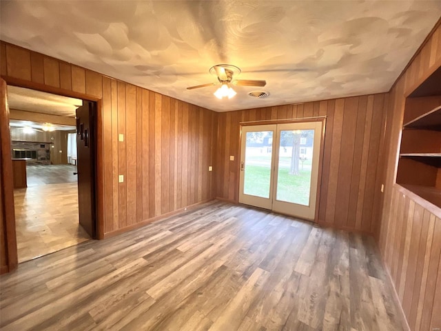 spare room with light hardwood / wood-style flooring, ceiling fan, and wooden walls