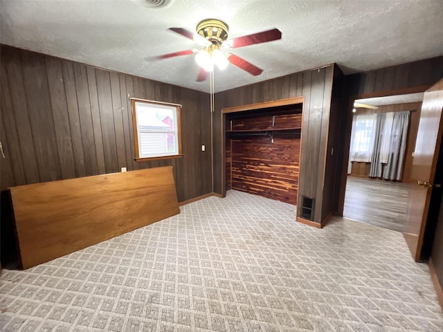 bedroom featuring wood walls, light carpet, ceiling fan, a textured ceiling, and a closet