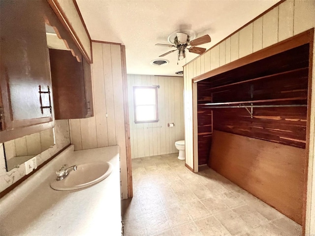 bathroom featuring vanity, toilet, ceiling fan, and wood walls