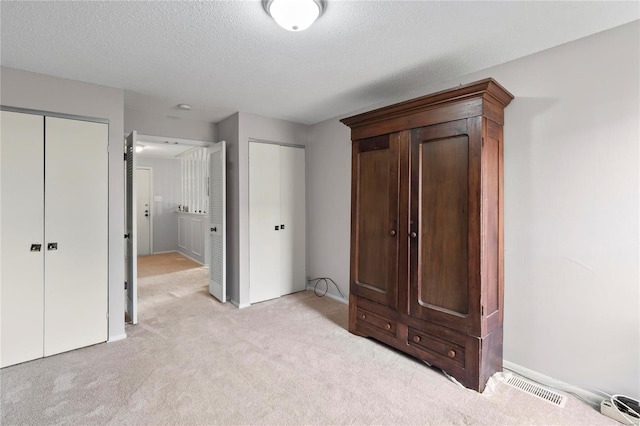 unfurnished bedroom featuring light carpet, a textured ceiling, and two closets